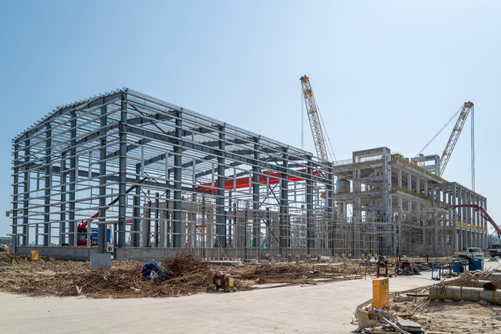 A steel building under construction with workers wearing safety gear and Canadian flags visible in the background.